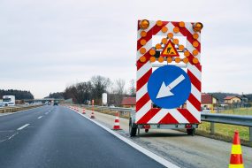 Foto: Roman Babakin Arrow down left reflective direction road sign in highway. Roadwork service signal. Narrow lane traffic indicator.