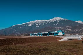 Modern slovenian double decker commuter train rushing through villages and rural areas towards city. Majestic mountain in the background.