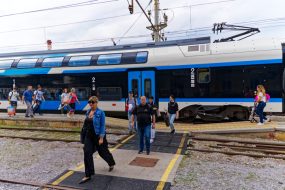 Scenic view of blue and white train at railway station of City of Skofja Loka with passengers leaving platform on a cloudy summer day. Photo taken August 9th, 2023, Škofja Loka, Slovenia.