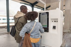 Travelers, African American couple buying tickets at a train station on a vending machine, paying with a payment card.